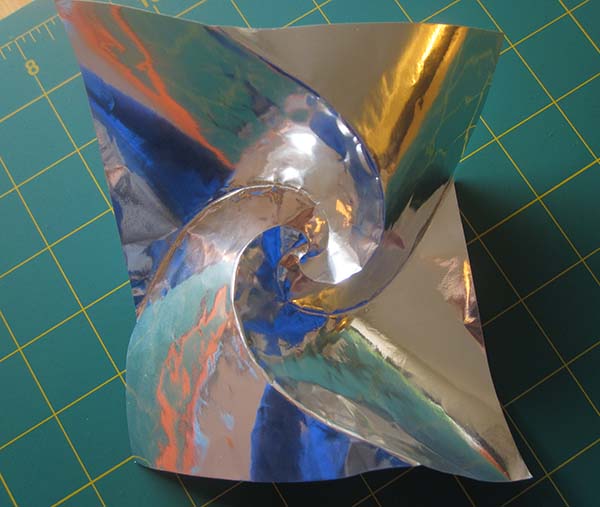 A square sheet of silver foil paper, with 4 spiral creases radiating from the center