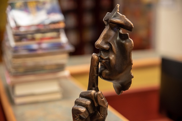 A bronze sculpture of a disembodied face with a finger to its lips