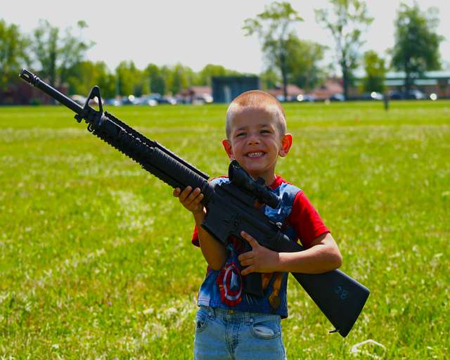 A small child holding a large assault rifle