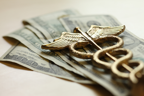 A medical caduceus laid on top of a stack of dollar bills