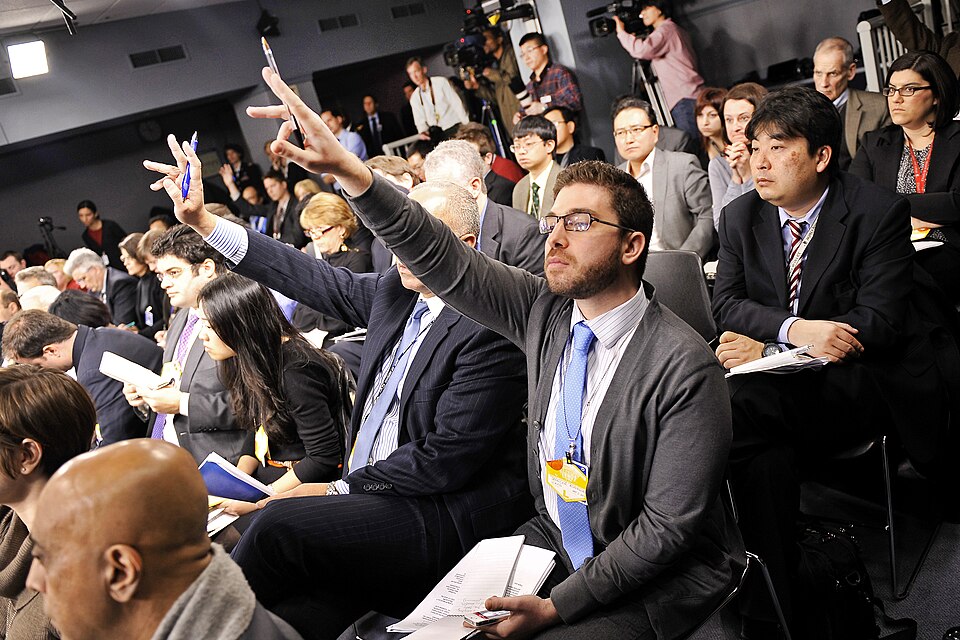 Members of the press raising their hands to ask questions