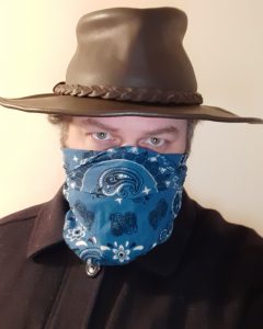 The image shows the author in his pandemic shopping outfit. He's wearing a dark navy blue wool jacket, a brown leather broadbrim hat, and a blue paisley bandanna covering his face below his eyes. 